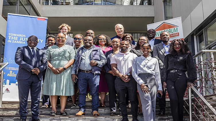 A diverse group of FES Partners smiling on steps outside a building. Banners read "Towards the Just City in Zambia" and "Civicforum". The mood is positive and collaborative.