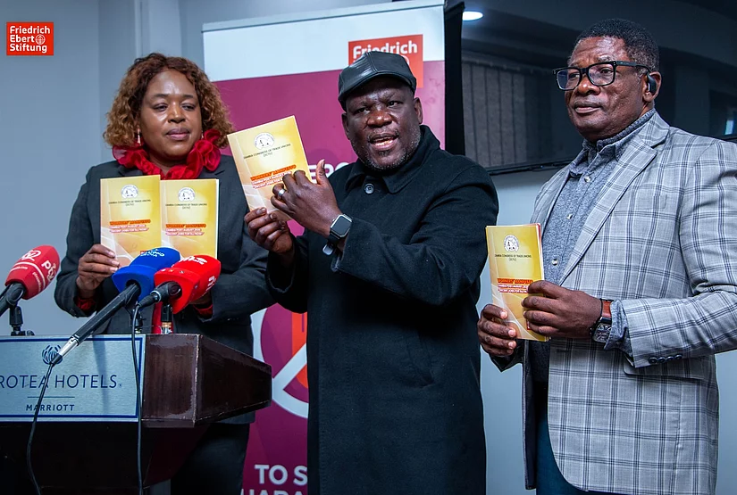 Three people holding Zambia Congress of Trade Unions document during a press event at Protea Hotels Marriott.