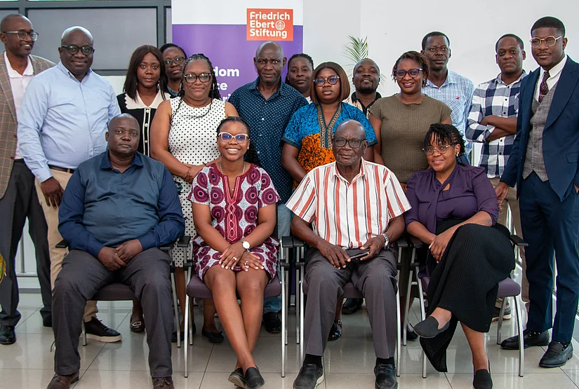 A group of African individuals, varying in age and gender, pose for a photo indoors. Many are seated in chairs arranged in front of a backdrop featuring the Friedrich Ebert Stiftung logo and text that includes "Freedom".
