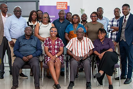 A group of African individuals, varying in age and gender, pose for a photo indoors. Many are seated in chairs arranged in front of a backdrop featuring the Friedrich Ebert Stiftung logo and text that includes "Freedom".