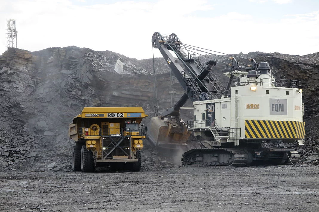 A large excavator loads rock into a dump truck at a quarry. The scene conveys industriousness, at a mine in Zambia and machinery under an overcast sky.